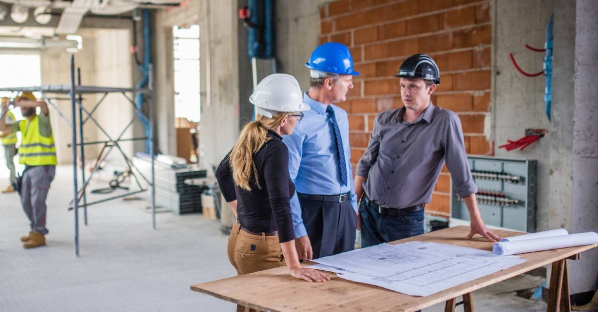 three people on construction site talking next to a table with plans on it